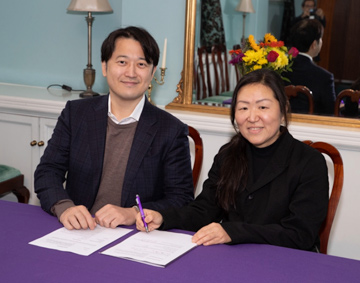 a man and woman sat at a desk signing a document