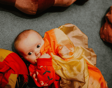 A baby lying on a blue carpet, hugging orange and yellow fabric