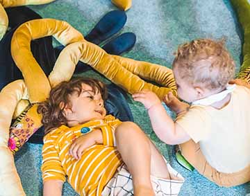 Two baby playing with soft toys and shapes on a blue carpet