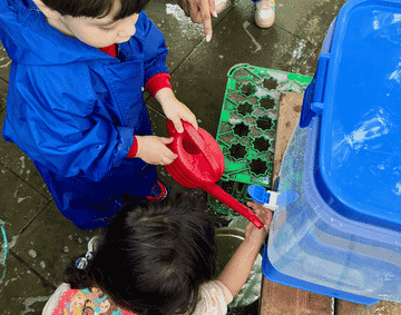 Two children filling up a watering can outside the gallery