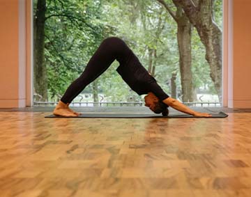 Pilates session at the Whitworth. A woman in a pilates pose, in a gallery space with a window behind her, overlooking some trees in a park. Photo courtesy of Pilates by Cordelia