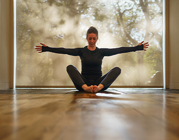 Pilates session at the Whitworth. A woman in a pilates pose, in a gallery space with a window behind her, overlooking some trees in a park. Photo courtesy of Pilates by Cordelia