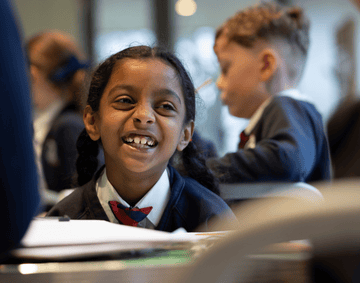 A smiling primary school students sat at a desk