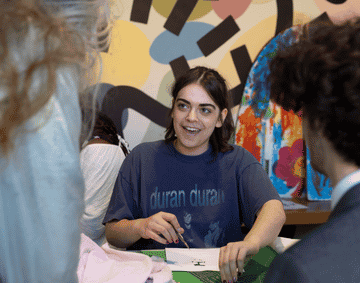 A student crafting on a green table against a multi-coloured background