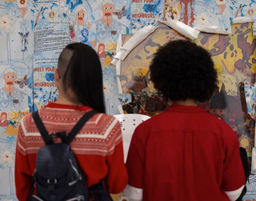 two peole facing a wall with artworks on it