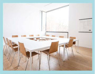 a meeting room with tables arranged in a square and on the far side a window flooding the space with light