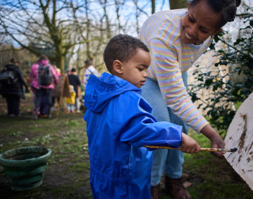 mother with her child who is painting at an easel in the outdoors