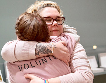 two people hugging, one is wearing a sweatshirt with Volunteer written on the back