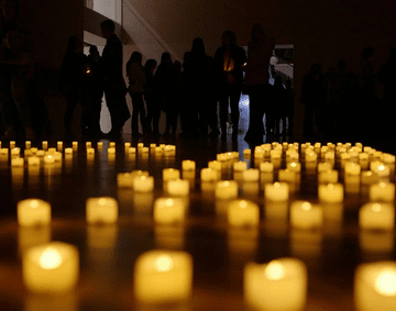 Candle lights on the floor, as people gather around in a dark room 