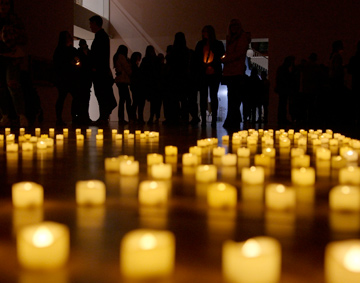 candles on the floor of a dark gallery space with figures in silhouette